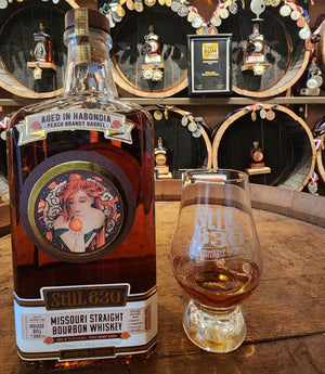 Missouri Straight Bourbon Whiskey bottle with a glass on a wooden surface, with decorative barrels in the background.